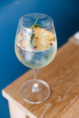 Cocktail in wine glass with dried slice pineapple and rosemary on the top.
