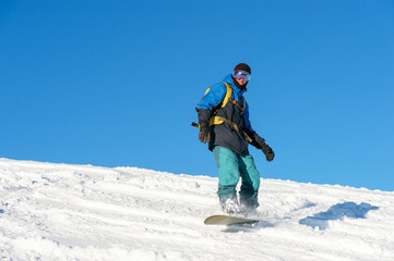 Fototapeta na wymiar Freeride snowboarder rolls on a snow-covered slope leaving behind a snow powder against the blue sky