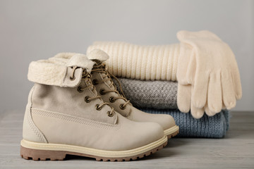 Leather women's light winter boots and a pile of knitted things (sweaters, scarves, gloves).