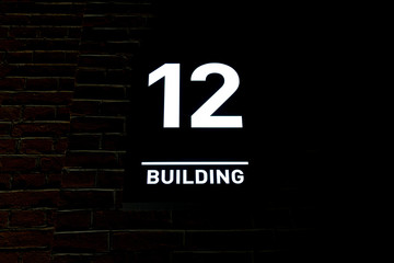 Luminous pointer with number 12 on the brick wall of the house
