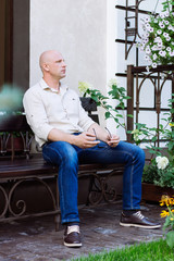 handsome man sit on the bench at garden with home background at spring time. green grass, jeans, shirt, summer