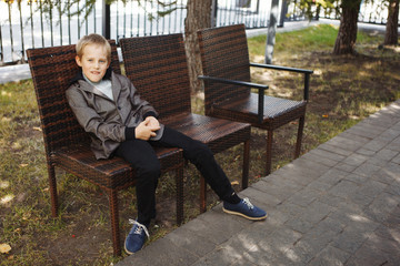 Fototapeta premium Handsome boy in a jacket, sitting on the bench looking at the Park on a Sunny fall day