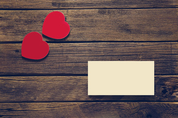two red hearts and a sheet of paper on a table of boards