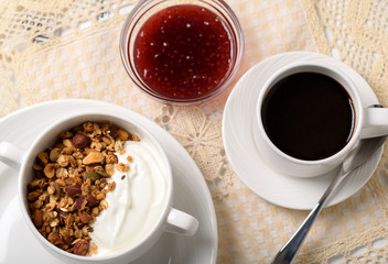 Obraz na płótnie Canvas Healthy breakfast: Greek yogurt with homemade granola in a white bowl, a cup of coffee and raspberry jam