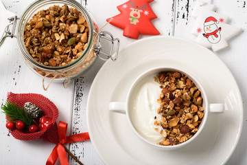 Healthy breakfast: Greek yogurt with homemade granola in a white bowl and jar with granola/ New year's decoration