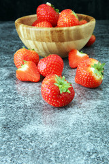 Fresh strawberries in a bowl and on grey background.