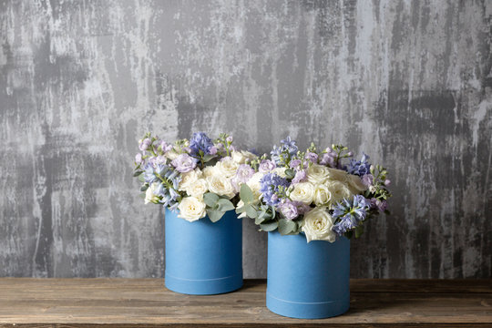 Fototapeta two flower bouquet in a hat box blue. standing on a wooden table. On the background old gray wall art. copy space.