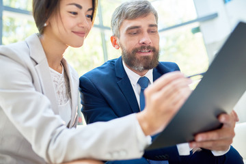 Fototapeta premium Portrait of two cheerful business people, young Asian woman and mature man, writing on clipboard planning projects in modern office