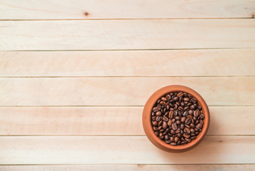 Clay pot with coffee beans on light wooden table. Menu design. Place for text. Top view.