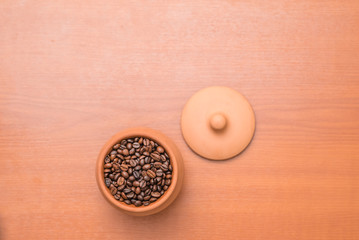 Clay pot with coffee beans on wooden table. Top view.