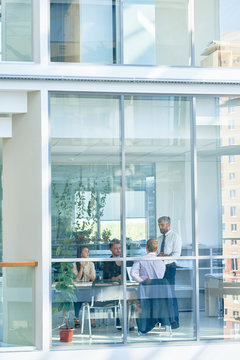 Wide Angle Of Business Meeting In Modern Office Behind Glass Windows, Shot From Outside Building