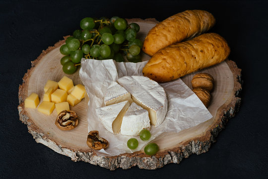 Cheese Camembert, bread, nuts and fruit on old wooden board. Food for wine and romantic, cheese and bread delicatessen. Menu design horizontal, side view.