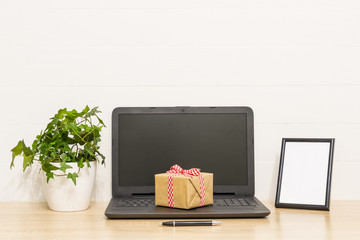 Laptop on wooden table with gift box, ivy plant in pot, photo frame, pen. Working space in loft. Interior photo