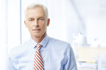 Financial business man. A senior financial consultant businessman standing in shirt and tie in his office.