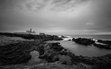 Long exposure from a lighthouse in a rocky beach in a cloudy winter day. Cascais, Portugal