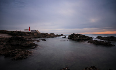 Fototapeta na wymiar Long exposure from a lighthouse in a rocky beach in a cloudy winter day. Cascais, Portugal