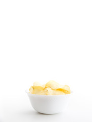 Crispy thinly sliced potato chips in white bowl, on white background.