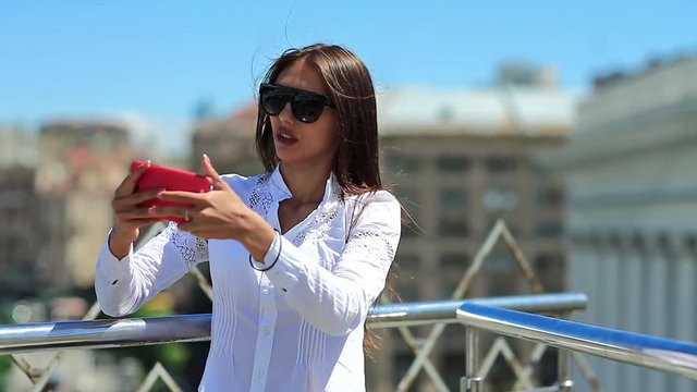 Attractive girl in sunglasses with red cell phone. Businesswoman makes selfie on his smartphone. Woman makes photos on mobile phone