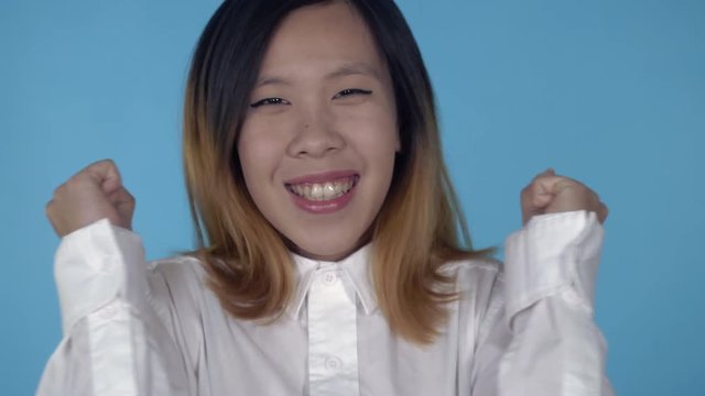 close up portrait young asian woman laughing celebrating success or good news or win her team on blue background in studio. attractive millennial girl looking at the camera