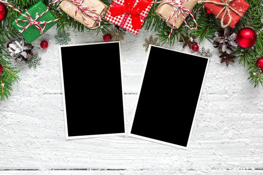 christmas blank photo frames with fir tree branches, decorations and gift boxes over white wooden background