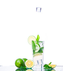 Ice cubes falls into Mojito cocktail with fresh lime, mint leaves and ice cubes in a transparent glass on a white background with reflection. Refreshing alcohol drink. Isolated on white background.