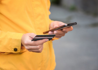 Young woman with credit card and mobile phone outdoors, closeup