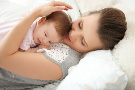 Young mother holding cute little baby on bed at home