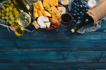 A large assortment of cheeses, wine, honey, nuts and spices, on a blue wooden table. Top view. Free space for text.