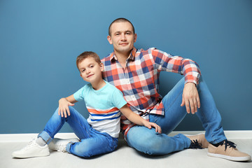 Fototapeta na wymiar Dad and his son sitting on floor near color wall