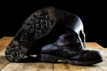 Muddy old military boots. Black color, dirty soles. Wooden table.