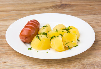 Fried sausage with boiled potatoes. A dish of boiled potatoes and fried sausages on a white plate.