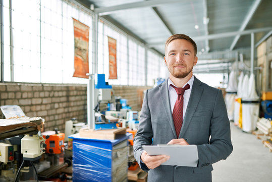 Portrait of successful sales assistant wearing suit posing looking at camera and smiling , standing in showroom selling industrial machine tools