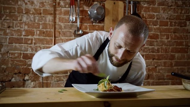 The professional male cook decorating the finished dish of potatoes, cream, herbs and cheese. 4K