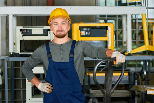 Portrait of cheerful young worker wearing hardhat posing looking at camera while working at modern factory workshop