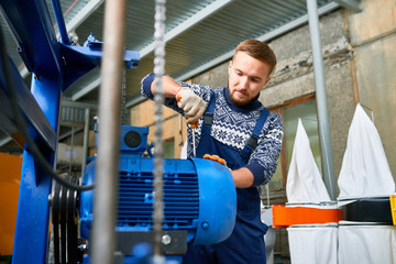 Portrait of  young man working at modern factory repairing machine units in industrial workshop, copy space