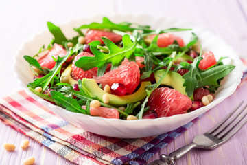 Fresh salad with arugula, grapefruit, avocado, pomegranate seeds and pine nuts.