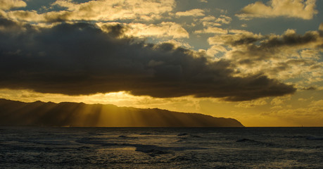 Dramatic sunset between clouds and Kaena Point on the north shore of Oahu, Hawaii