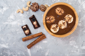 Chocolate smoothie on a wooden bowl with banana and nuts on grey  background, top view