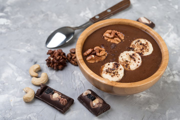 Chocolate smoothie on a bowl with banana and nuts on grey stone  background