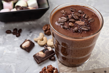 Chocolate smoothie on a glass with coffee beans and nuts on grey stone  background