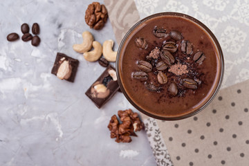 Chocolate smoothie on a glass with coffee beans and nuts on grey stone  background