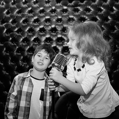 Singing little children with a microphone on a rack against a black wall