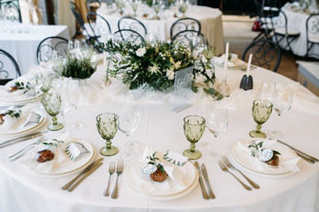 Decorated tables with plates, knives, forks and bouquet with white flowers and greens on the centre
