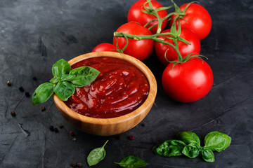 Tomato ketchup sauce in a wood  bowl with  herbs and  tomatoes on dark background.