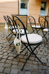 Decorated outdoor wedding ceremony with white wrought-iron chairs and rose petals in paper packets