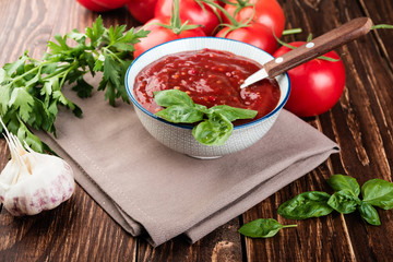 Tomato ketchup sauce in a   bowl with  herbs and  tomatoes on rustic background.