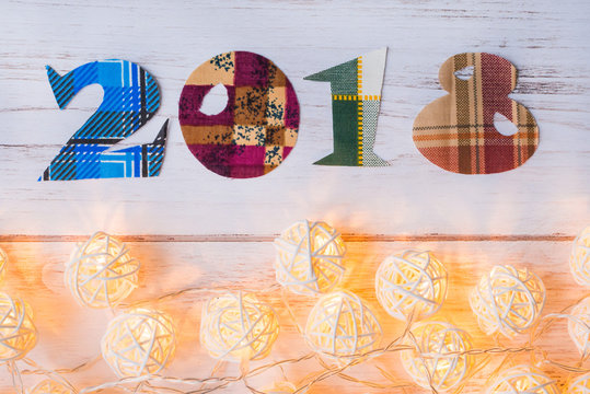 The inscription two thousand eighteen cut from fabric and Christmas illuminated garland