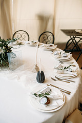 Decorated tables with plates, knives, forks and bouquet with white flowers and greens on the centre