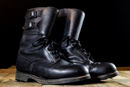 Old black Polish military boots on a wooden table.