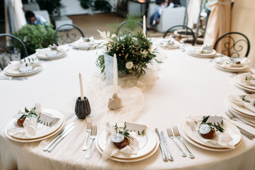 Decorated tables with plates, knives, forks and bouquet with white flowers and greens on the centre